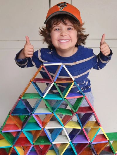 Photo of smiling boy giving two thumbs up, proud of the pyramid he has built with blocks