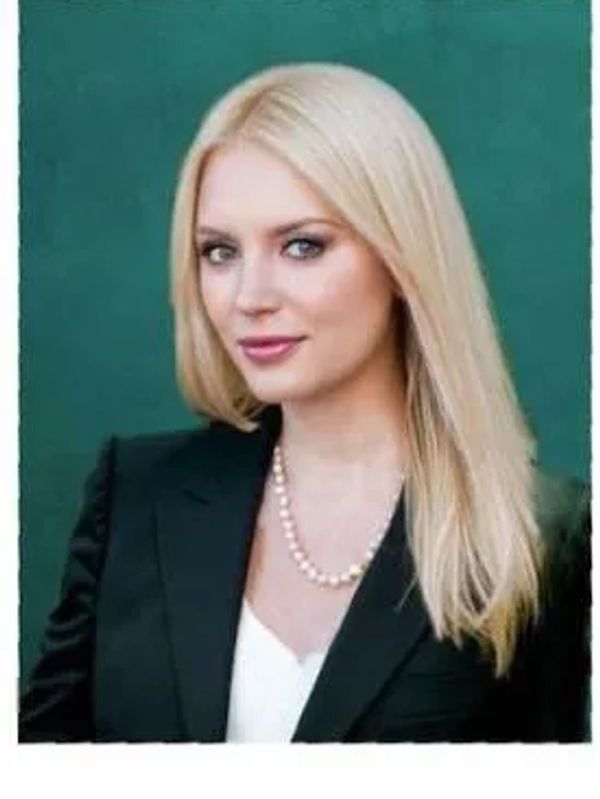 Professional woman with blonde hair in black blazer and pearls.