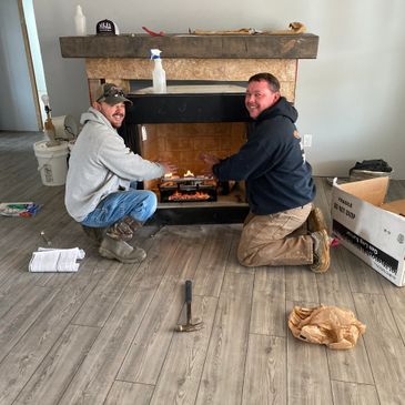 Two men warming hands by a fireplace in an unfinished room.
