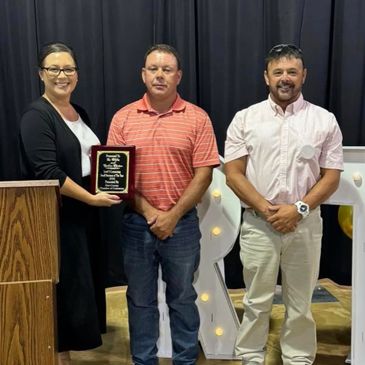 Three people stand in front of a black curtain, one holding an award plaque.
