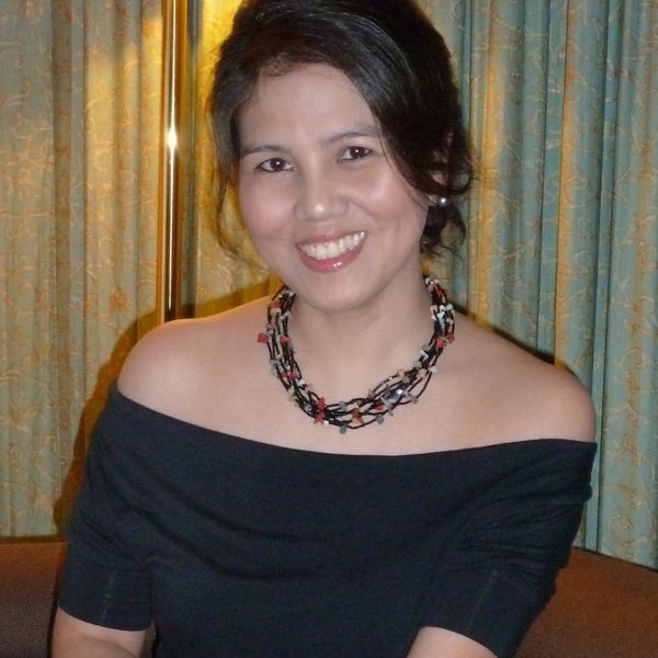 Smiling woman in an off-shoulder black top and beaded necklace.