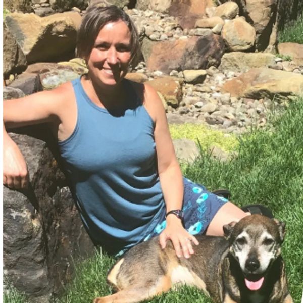 Woman in blue top sitting on grass petting a happy dog.