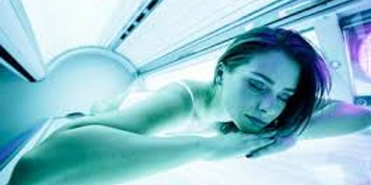 Young woman laying inside a tanning bed with eyes closed.
