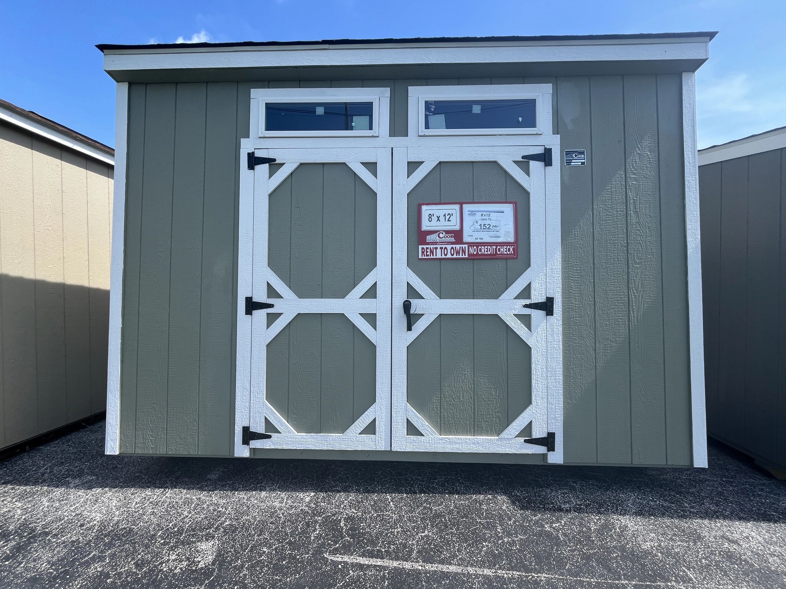 Green and white storage shed with "Rent to Own" sign on doors.