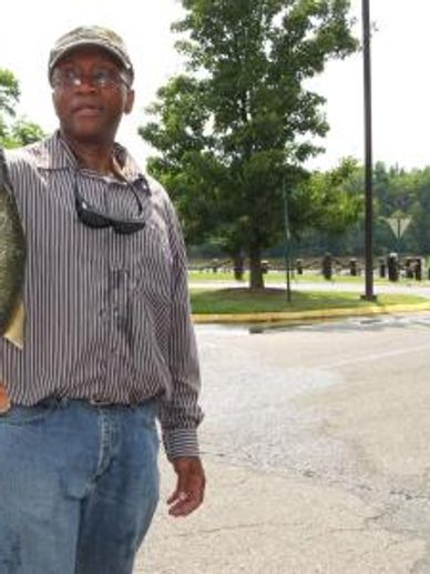 Man holding a fish outdoors near a parking lot and trees.