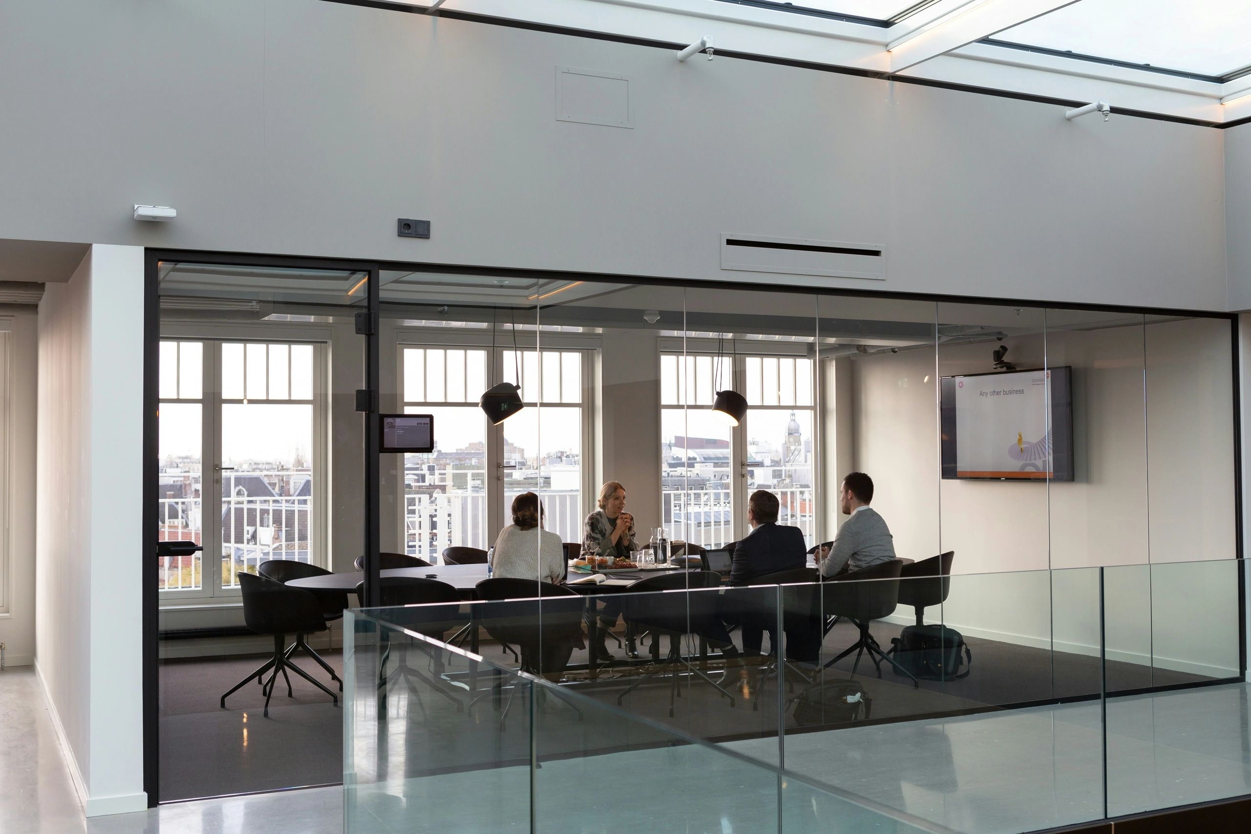 Four people having a meeting in a modern glass-walled conference room.