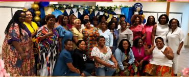 Group of women smiling at a festive indoor gathering with balloons and decorations.
