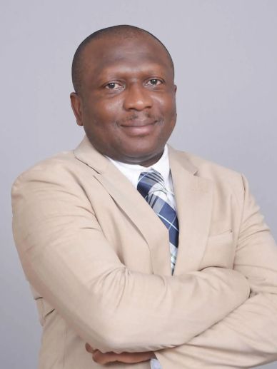 Confident man in beige suit with crossed arms and a slight smile.