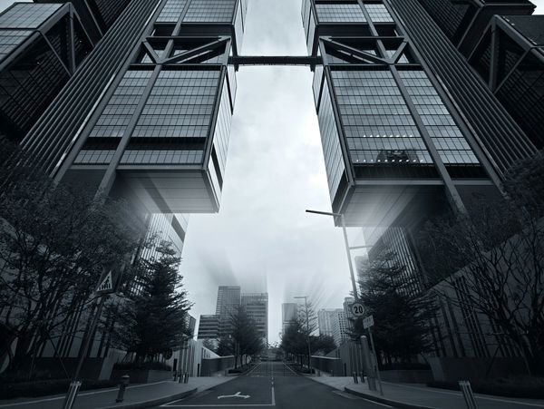 Symmetrical modern skyscrapers towering over an empty city street in monochrome.