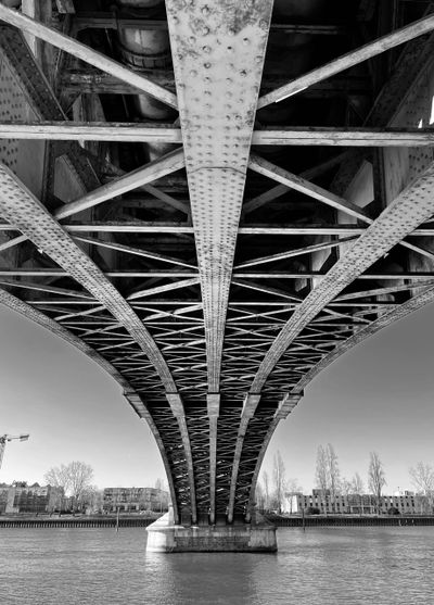 Black and white photo of a steel bridge's underside over a river.