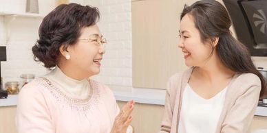Two women smiling and chatting indoors, enjoying a pleasant conversation.