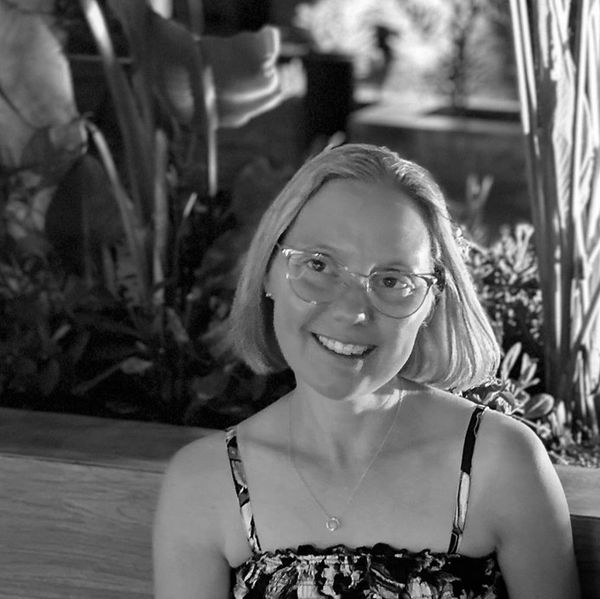 Smiling woman with glasses in a relaxed outdoor setting.