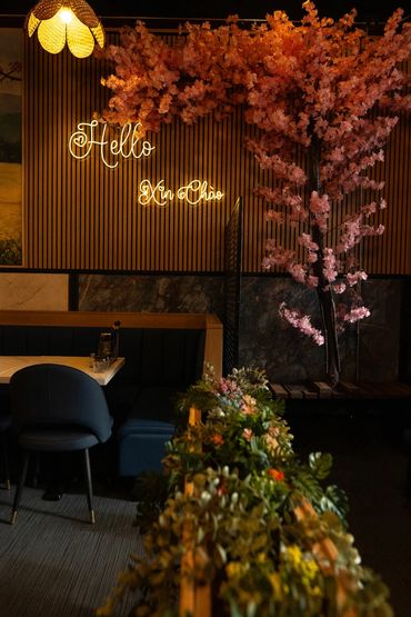 Cozy indoor seating with pink cherry blossoms and neon 'Hello Xin Chao' sign.