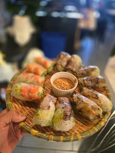 Hand holding a basket of fresh spring rolls with dipping sauce.