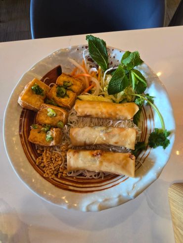 A plate with spring rolls, tofu, noodles, and fresh herbs.
