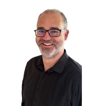 Smiling man with glasses and beard in a black shirt.