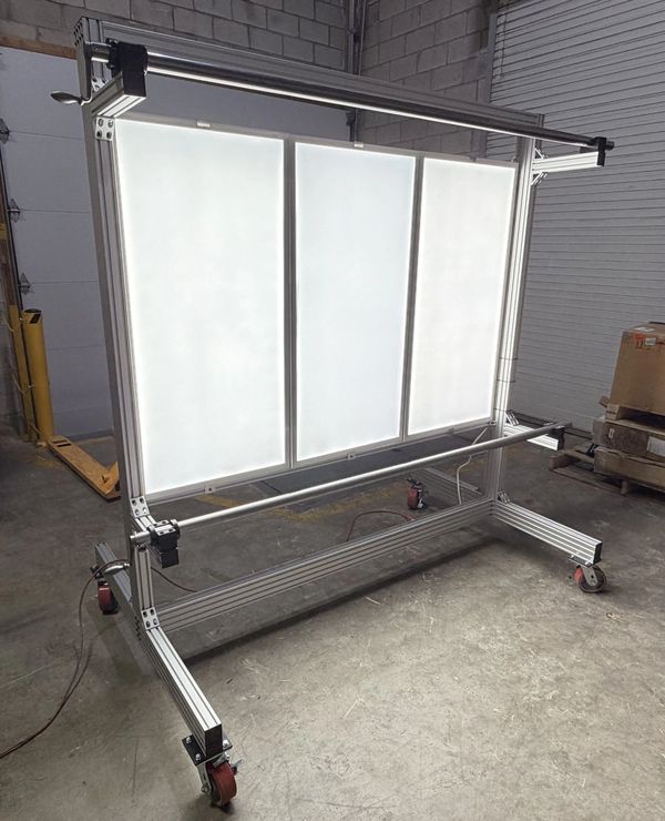 A large, portable light panel with aluminum frame on wheels in an industrial setting.