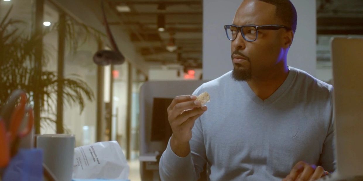 Man in glasses eating a snack in an office setting.