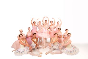 Group of ballerinas in pink and floral tutus posing together.