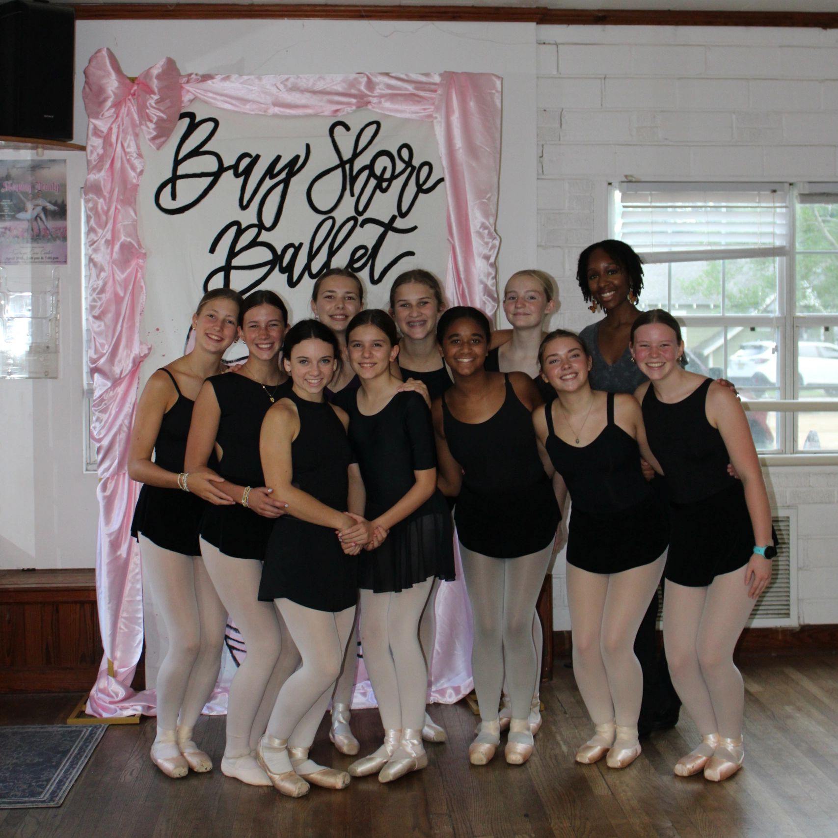 A joyful group of young ballet dancers posing in front of a Bay Shore Ballet sign.