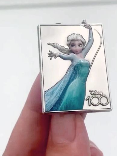 A hand holding a Disney 100 Elsa pin from Frozen.
