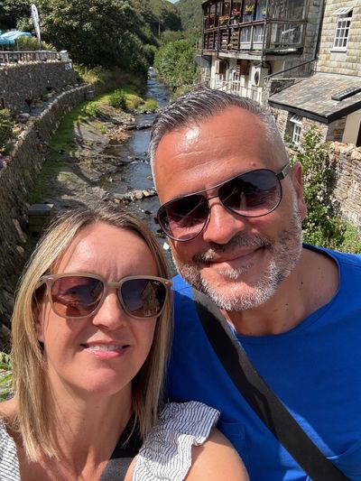 Couple wearing sunglasses smiling near a scenic river.