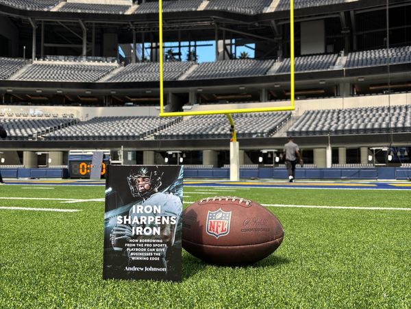 A football and a book titled 'Iron Sharpens Iron' on a stadium field near the goalpost.