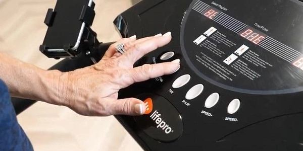 A hand pressing a button on the panel of a Lifepro Rhythm Vibration Platform
