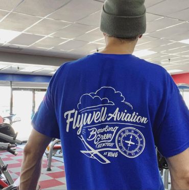 Person wearing a blue Flywell Aviation shirt in a gym.