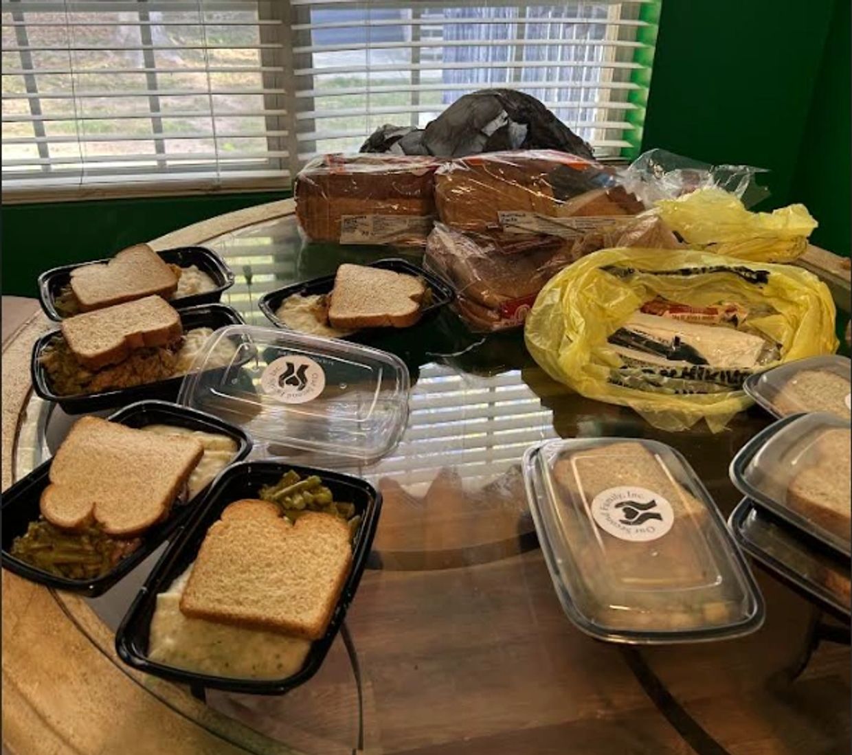 Multiple prepared meal trays with bread on a glass table.