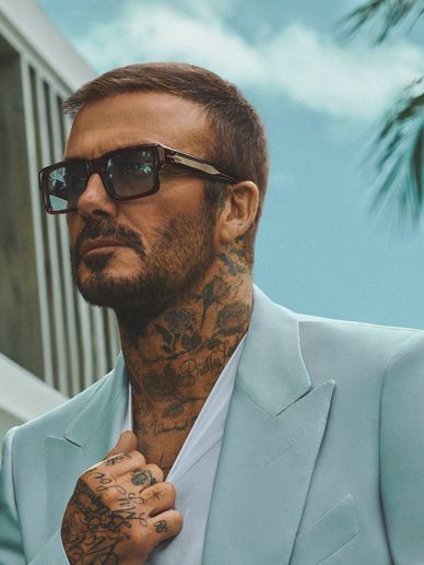 Man in light blue suit with tattoos and sunglasses.