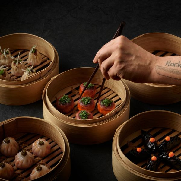 Hand using chopsticks to pick dumplings from bamboo steamers.