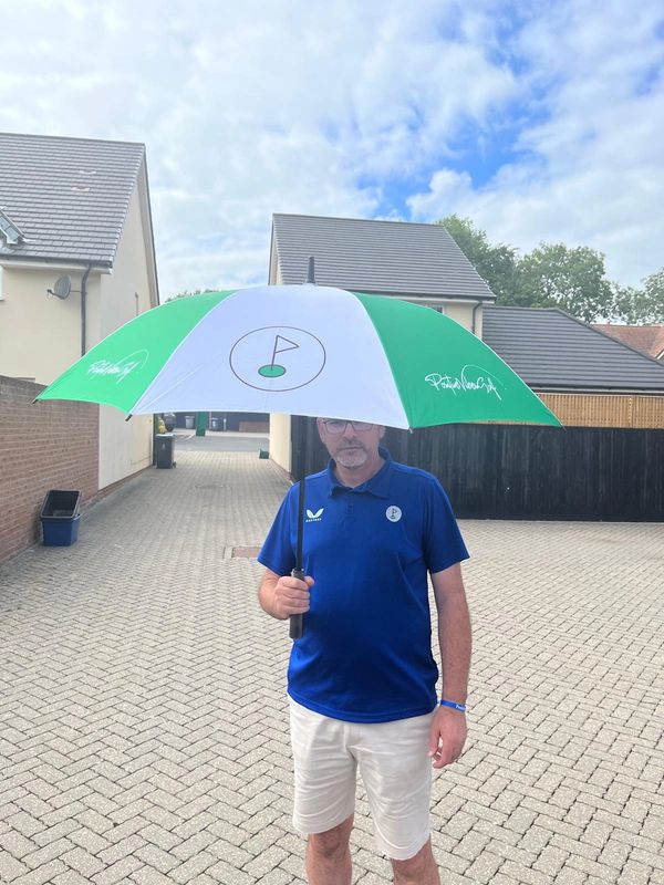 Man standing outdoors holding a green and white umbrella with a golf flag design.