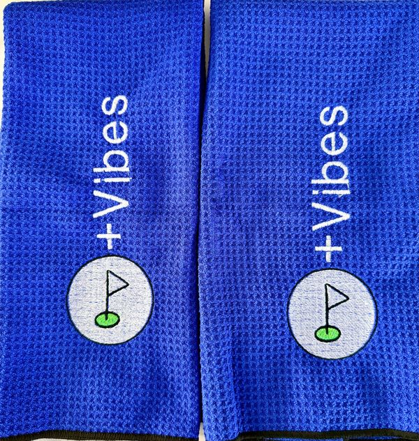 Two blue towels with +Vibes and golf flag designs.