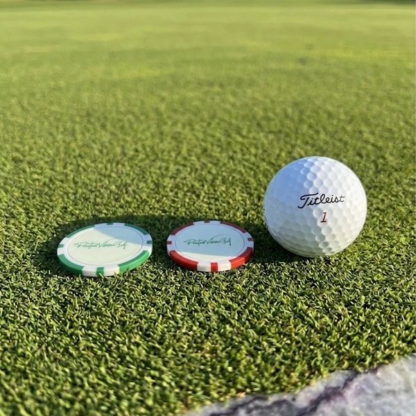A golf ball and two poker chips on green grass.