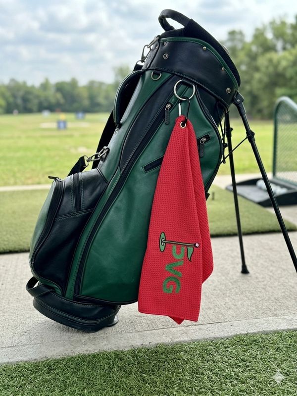 Green and black golf bag with a red towel hanging on it at a golf range.
