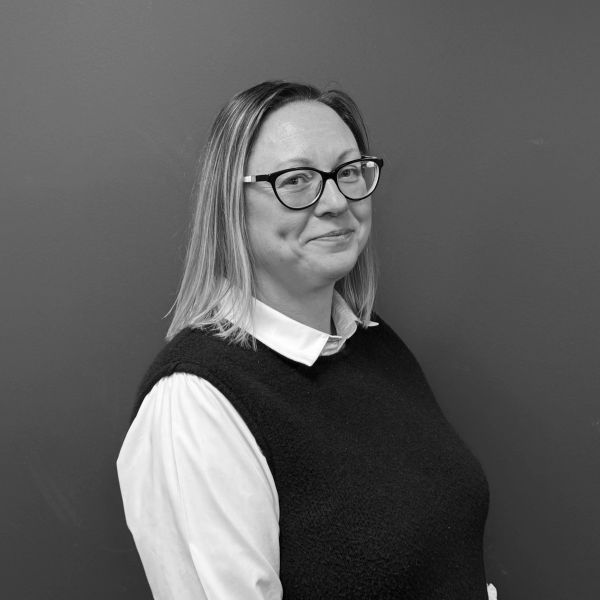 Woman with glasses smiling against a plain background.