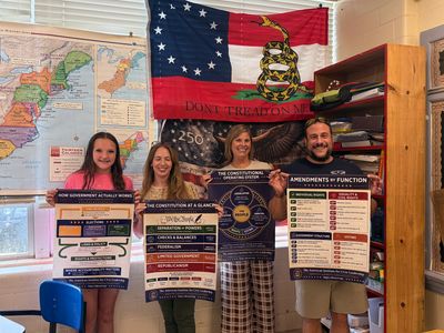 Four people hold posters about government and constitution in a classroom.