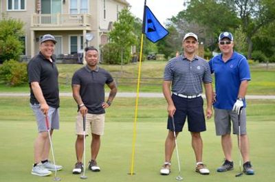 Four men posing on a golf green by a blue flag
