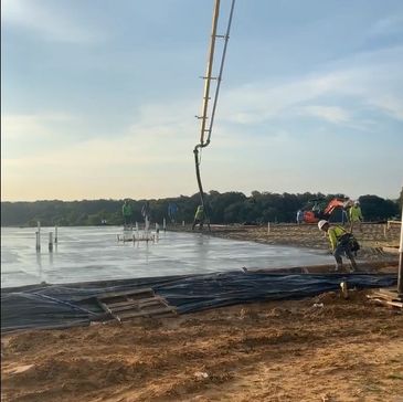 Workers pouring concrete on a construction site under a clear sky.