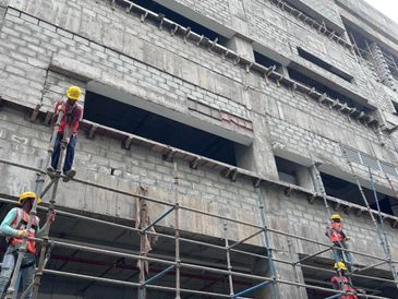 Construction workers on scaffolding at a building site wearing safety gear.