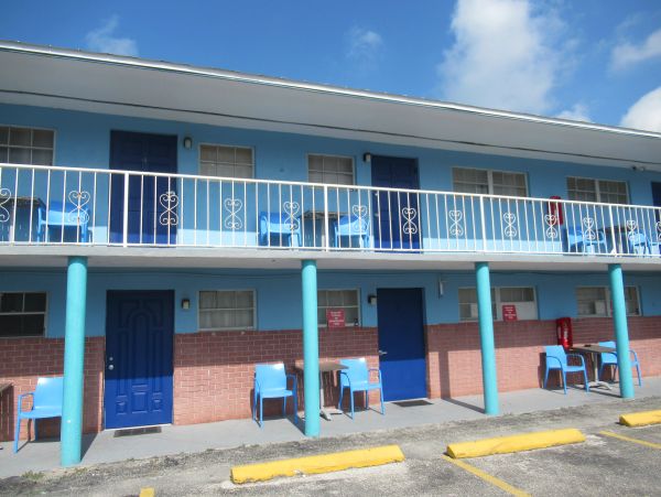Blue and pink motel with blue doors and chairs outside rooms.