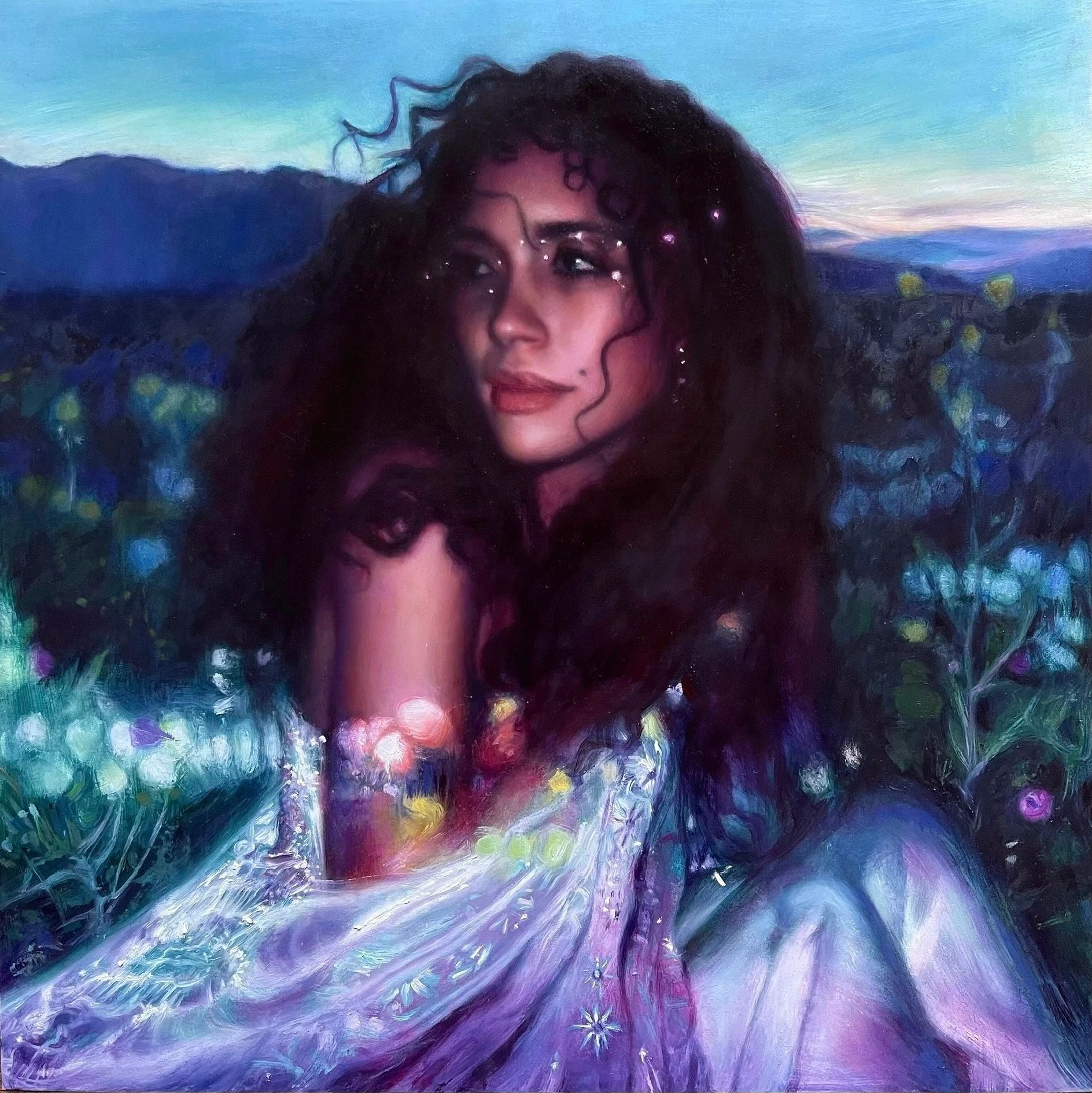 Woman with curly hair in a glowing dress amid flowers at dusk.