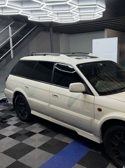 White station wagon with black wheels parked indoors under hexagonal lights.