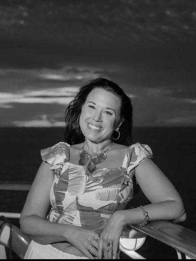 Woman smiling on a deck with a sunset over the ocean in the background.
