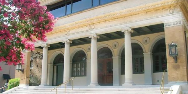 Historic building entrance with columns and pink flowers.