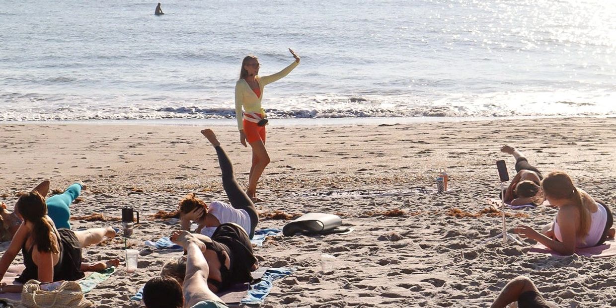 Group doing yoga on the beach with instructor and ocean background.