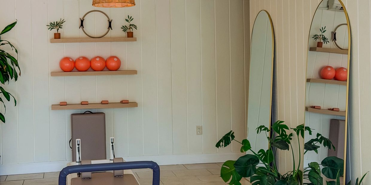 Minimalist home gym with reformer, plants, and decorative shelves.