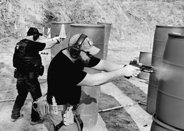 Two men shooting at a gun range with barriers.