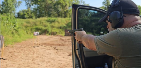 Person shooting a handgun at a target at an outdoor range.